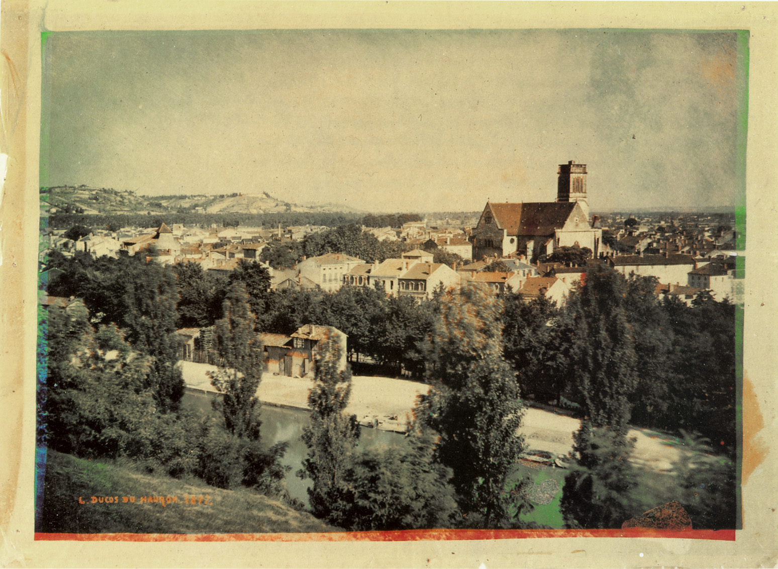 a trichromy by Ducos du Hauron showing a village surrounded by trees, with a church at its center.